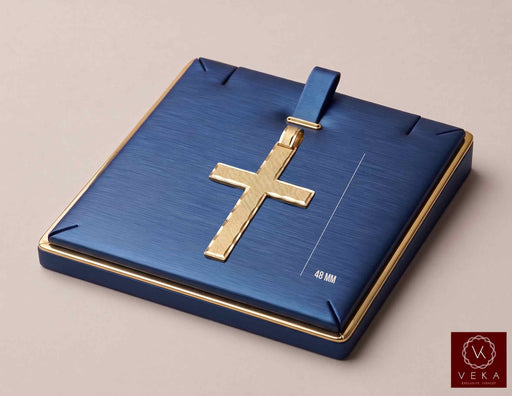 A 10K Real gold cross pendant displayed on a square textured blue jewelry box with gold trim, set against a solid beige background. A Veka Jewelry logo is visible in the bottom right corner.