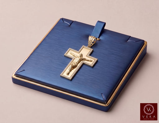 A 10K gold crucifix pendant with a detailed figure of Jesus, set against a textured blue presentation box with gold trim, on a neutral beige background with Veka Jewelry