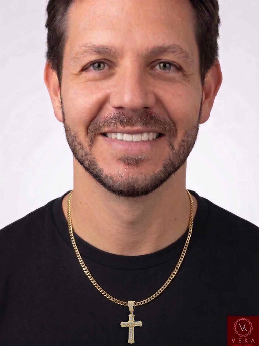 A smiling man with short brown hair and a trimmed beard, wearing a black crew-neck t-shirt and a gold chain necklace with a 10K Yellow Gold 0.45 CTW Natural Diamond Flared Cross Pendant, set against a plain light gray background with Veka Jewelry logo