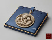 A custom circular family portrait pendant displayed on its blue presentation box. The 10 Karat Real gold pendant adorned with zirconia stones all around nad the bail features a sepia-toned photo of a grandfather, father, and daughter, surrounded by a gold-toned beaded border and a blue ribbon loop.