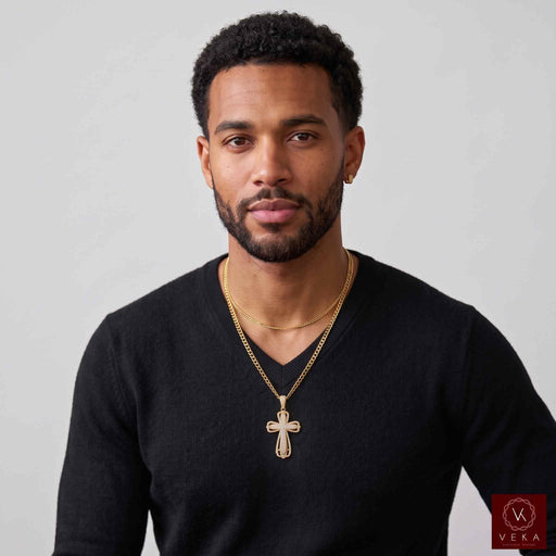 A man wearing a black v-neck sweater and a 10K gold cross pendant necklace, shown from the chest up against a light gray background. A small Veka Jewelry logo watermark is visible in the bottom right corner.