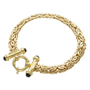 10K yellow gold Byzantine bracelet with a round clasp displayed on a professional jewelry display tray with perfume bottles in the background.