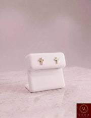 Pair of Veka Jewelry 10K solid yellow gold cross stud earrings featuring 1/10 ctw genuine natural diamonds, elegantly displayed on a white leather stand.