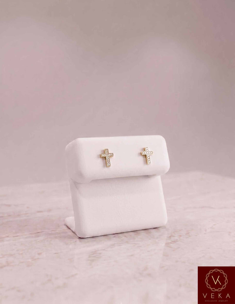 Pair of Veka Jewelry 10K solid yellow gold cross stud earrings featuring 1/10 ctw genuine natural diamonds, elegantly displayed on a white leather stand.