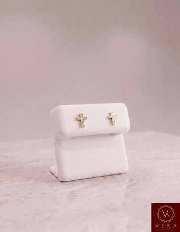 Pair of Veka Jewelry 10K solid yellow gold cross stud earrings featuring 1/10 ctw genuine natural diamonds, elegantly displayed on a white leather stand.