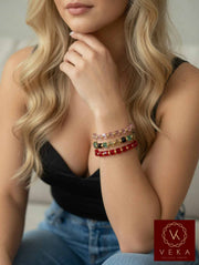 Blonde woman wearing stack of 10K yellow gold Swarovski crystal adjustable macrame bracelets in pink, multicolor, and red on her wrist