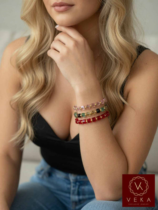 Blonde woman wearing stack of 10K yellow gold Swarovski crystal adjustable macrame bracelets in pink, multicolor, and red on her wrist