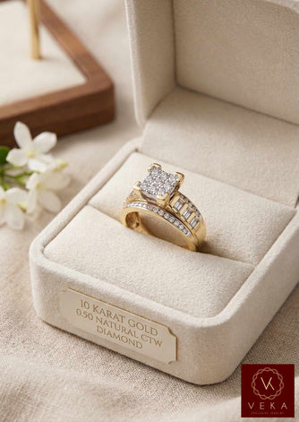 A high-angle view of the VEKA Cinderella style 10k yellow gold engagement ring. The ring, which features a cluster setting of round and baguette diamonds and a split-shank integrated band, is presented in a premium beige velvet ring box on a linen background. The front of the box has a plaque engraved with 