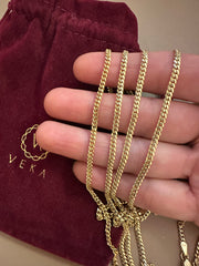 Gold chain held by a hand with a burgundy pouch featuring 'VEKA' branding in the background.