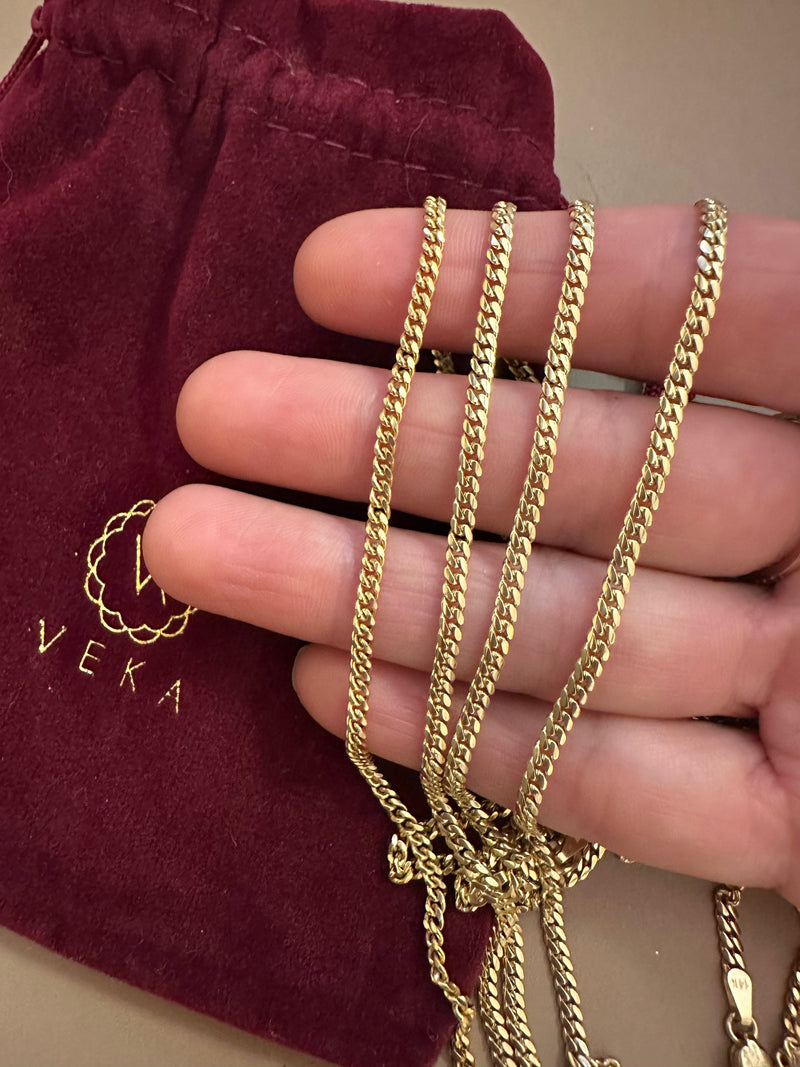 Gold chain held by a hand with a burgundy pouch featuring 'VEKA' branding in the background.