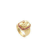 A close-up view of a 14K yellow gold Saint Barbara religious signet ring, detailed with red synthetic rubies, resting on a white background.
