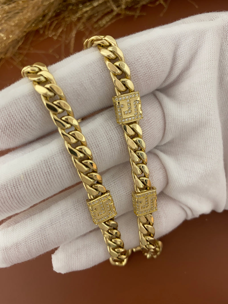 14K yellow gold curb link bracelet featuring geometric maze pattern stations encrusted with clear cubic zirconia stones and a large spring ring clasp on a hand with a earth color background.