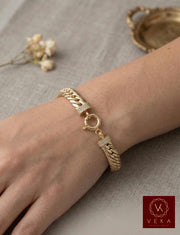 Close-up of a woman's wrist wearing an 8.5mm wide 14K yellow gold link bracelet with a decorative round lock and zirconia accents, featuring the VEKA Jewelry logo.