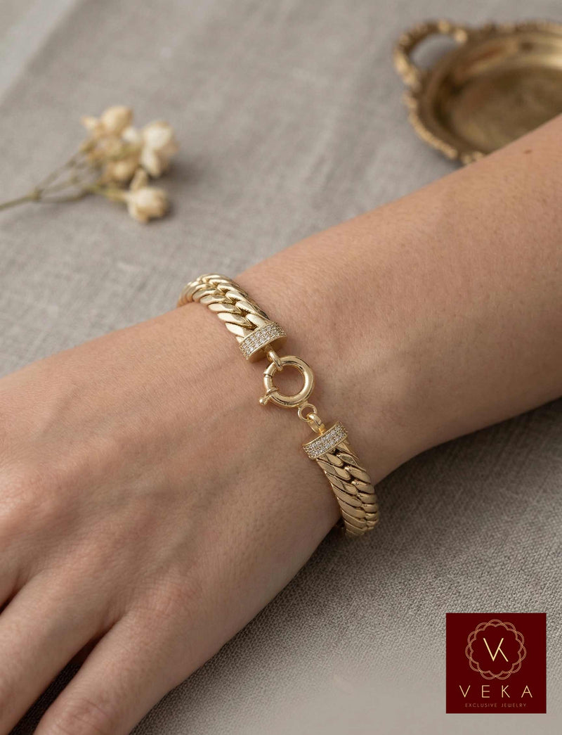 Close-up of a woman's wrist wearing an 8.5mm wide 14K yellow gold link bracelet with a decorative round lock and zirconia accents, featuring the VEKA Jewelry logo.