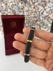 Close-up of 14K solid gold braided black leather men's bracelet held in hand showing gold details and braided texture