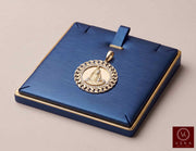 14K yellow gold Caridad del Cobre medal pendant with CZ Cuban link border displayed on a luxury navy blue jewelry tray by Veka Jewelry