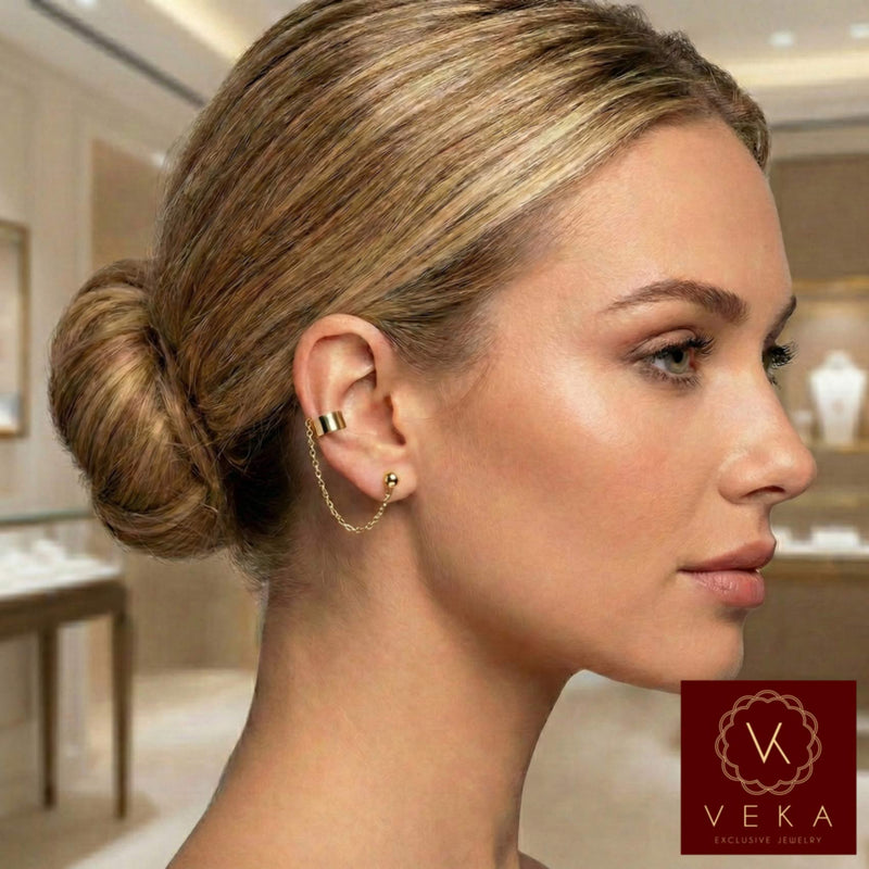 Model wearing a 14K yellow gold ear cuff connected to a ball stud earring by a delicate gold chain. Stylish helix-to-lobe jewelry by VEKA Jewelry.