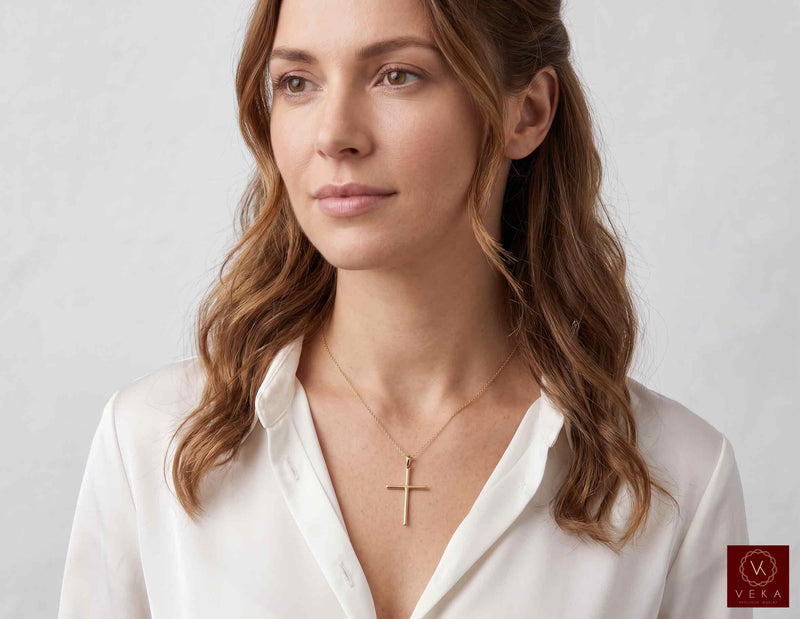 Female model wearing 14K yellow gold slim minimalist cross pendant on a delicate chain with white shirt