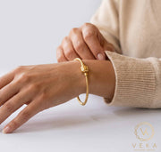 Woman wearing 14K yellow gold 2.5mm snake chain charm bracelet on wrist over neutral grey background - fine jewelry lifestyle by Veka Jewelry.
