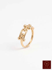 A 14k Interlocking gold ring with an abstract, organic chain-like design accented by small metallic beads, shown on a clean white background with a Veka logo in the bottom right corner.