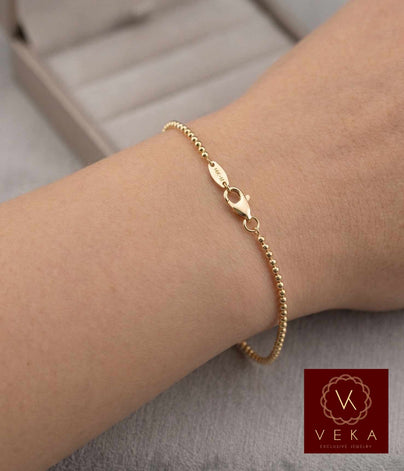 Close-up view of a high-polished 2mm Moon Bead bracelet made of 14K solid yellow gold, showing the secure lobster clasp, worn on a woman's wrist.