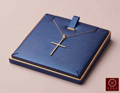 14K solid yellow gold slim cross pendant displayed on a navy blue jewelry tray with delicate gold chain by Veka Jewelry