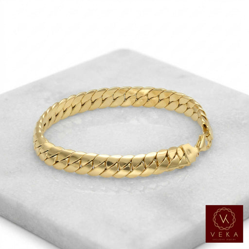 Professional studio shot of a 14k yellow gold 8.5mm Italian tight Cuban link bracelet showcased on a white marble pedestal, luxury fine jewelry by Veka