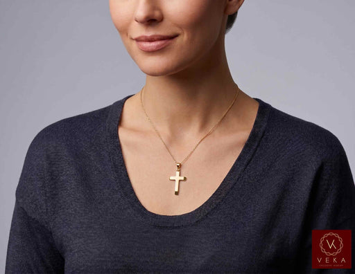 Woman wearing the 14K yellow gold beveled cross pendant on a gold chain necklace by Veka Jewelry.