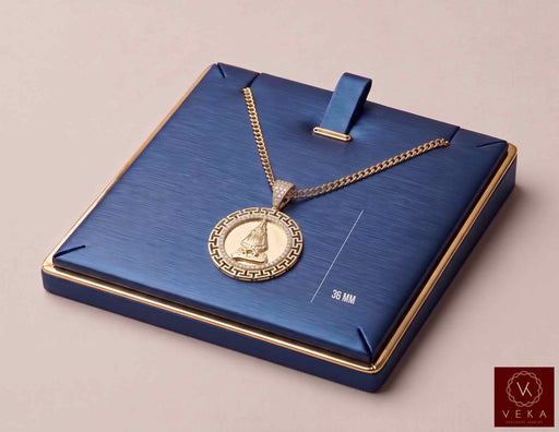 14K yellow gold Caridad del Cobre medal pendant displayed on navy blue jewelry board with gold chain by Veka Jewelry