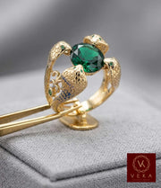 Close-up of a 14K yellow gold ring featuring four textured cobra heads holding a large oval emerald green zirconia stone