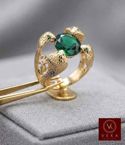 Close-up of a 14K yellow gold ring featuring four textured cobra heads holding a large oval emerald green zirconia stone