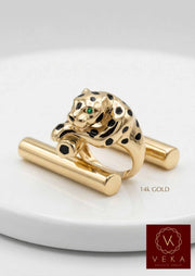 Front view of a 14k solid yellow gold panther statement ring with black enamel spots and emerald green cubic zirconia eyes on a white pedestal