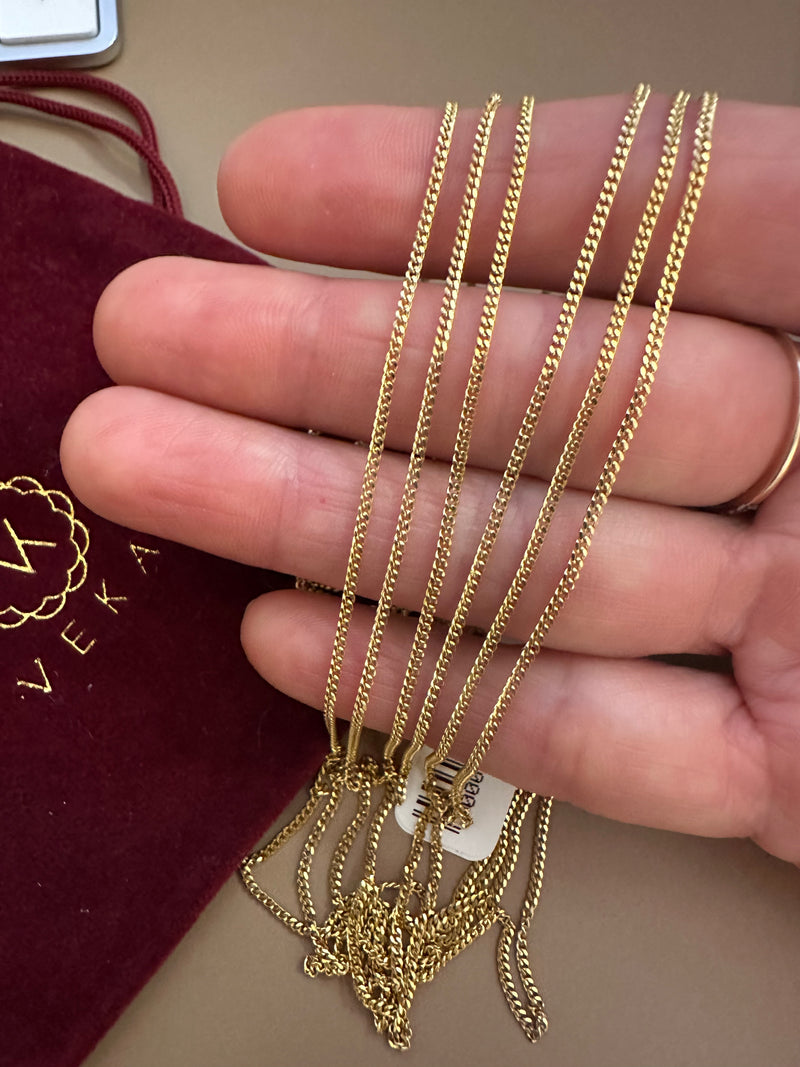 Gold chains held by a hand with a Veka brand label in the background
