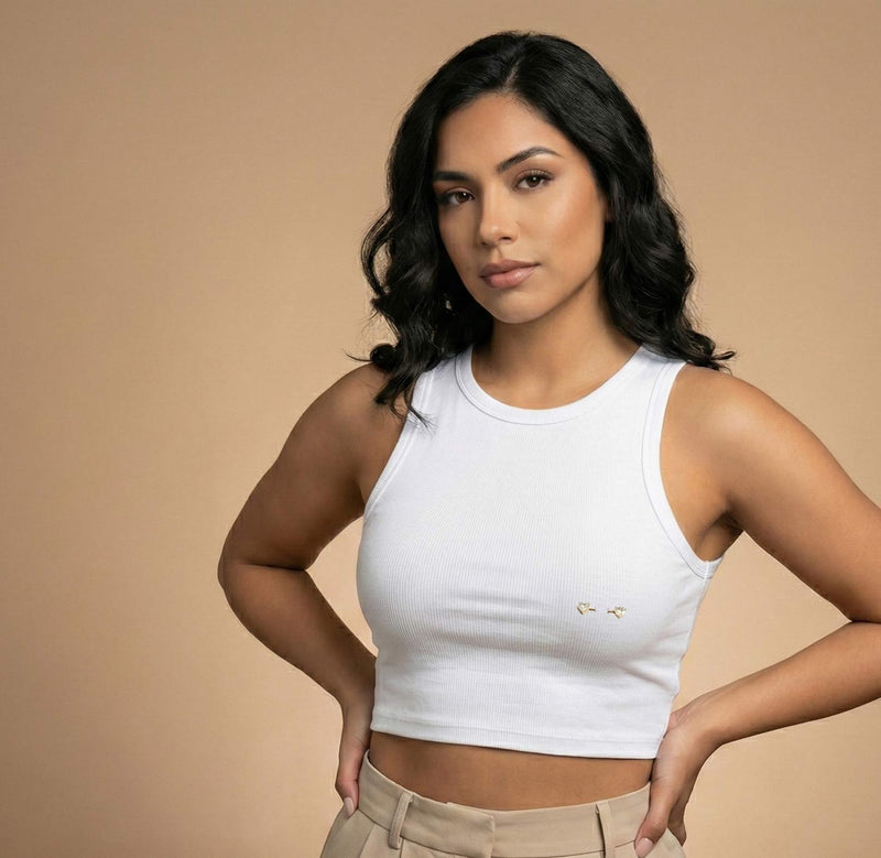Woman wearing a white tank top against a beige background and a nipple piercing
