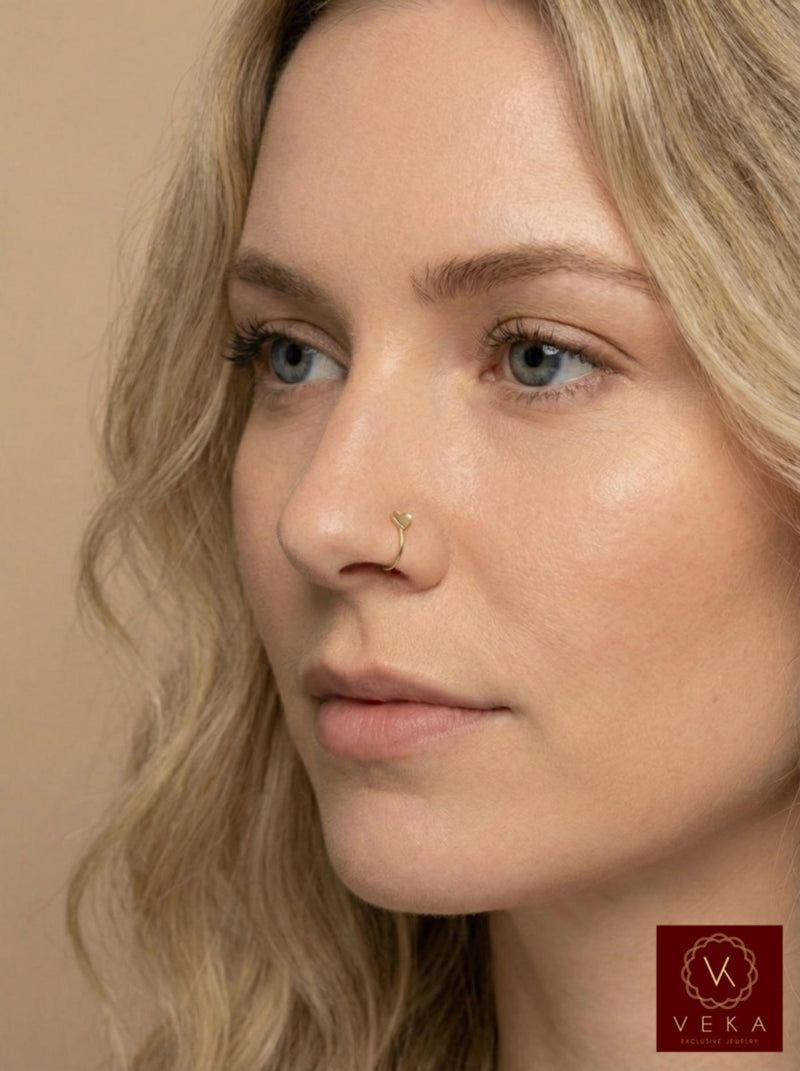 Close-up of a model wearing a 14k gold open nose hoop with a tiny heart detail. Dainty gold nostril piercing jewelry by VEKA Jewelry