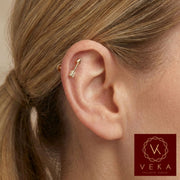 Close-up profile of a blonde woman wearing a small 14k yellow gold arrow flat back stud in an upper helix cartilage piercing. Dainty gold ear jewelry by VEKA Jewelry.