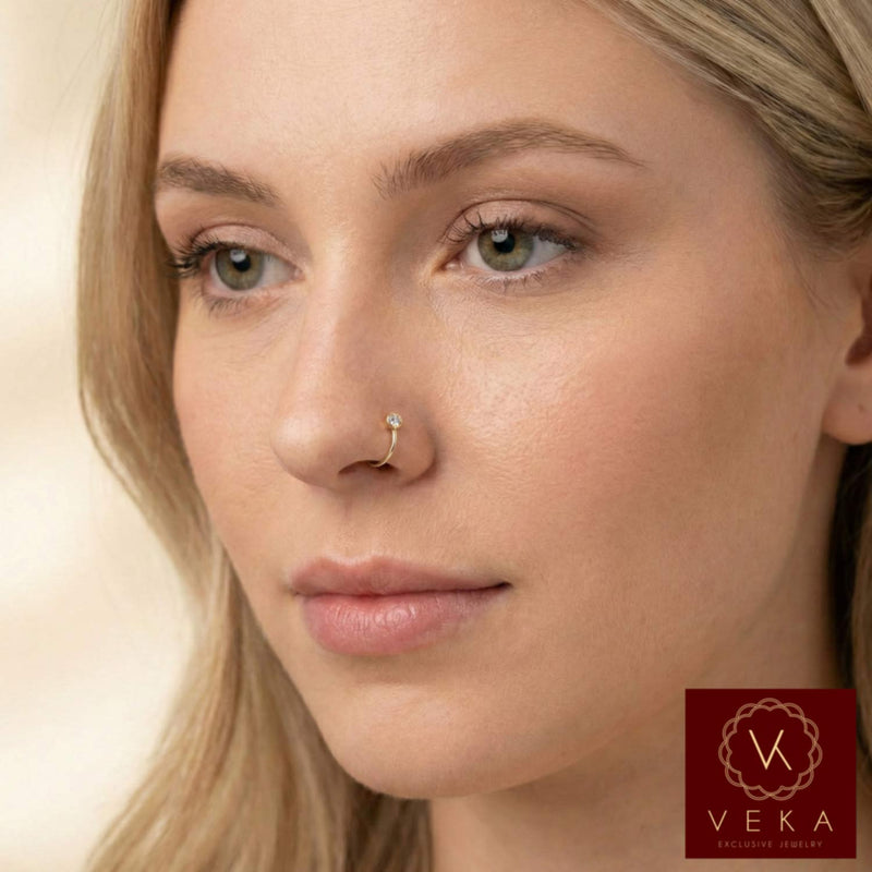 Close up of a woman wearing a minimalist 14k yellow gold nose hoop with a tiny bezel set stone. The ring is 24 gauge and 9mm diameter, sold by VEKA Jewelry.