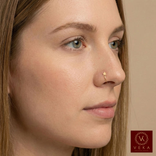 Close-up of a woman's face with a 14k yellow gold open nose hoop featuring a tiny star accent. Minimalist gold nose piercing jewelry by VEKA Jewelry
