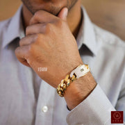 A close-up of a man's wrist wearing a gold-toned 15 mm Monaco Mens Bracelet CLASSIC Pave Lock 14K Gold, over a light blue striped dress shirt.