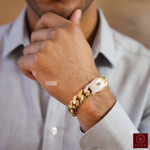 A close-up of a man's wrist wearing a gold-toned 15 mm Monaco Mens Bracelet CLASSIC Pave Lock 14K Gold, over a light blue striped dress shirt.