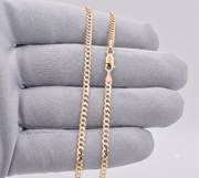Close-up of 2.5mm solid 14k gold Italian curb link chain held in a gray gloved hand showing lobster claw lock and 10k stamp