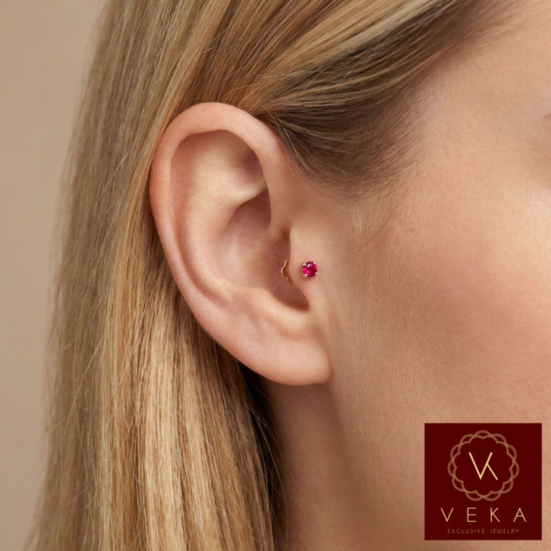 Close-up profile of a blonde woman wearing a small 14k yellow gold and synthetic ruby flat back stud in a tragus cartilage piercing. Dainty minimalist ear jewelry by VEKA Jewelry