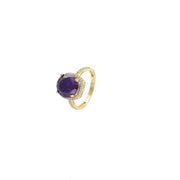 Synthetic Amethyst Stone on top a yellow real gold ring set on a top side view angle. The purple stone is set in 4 prongs, and the base is surrounded by cubic clear zirconium stones. 