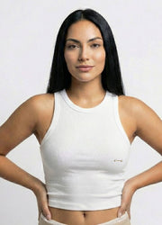 Woman wearing a white tank with a nipple barbell piercing top against a plain background