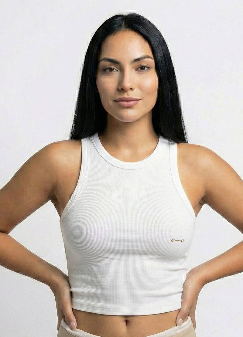 Woman wearing a white tank with a nipple barbell piercing top against a plain background