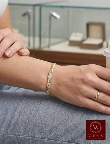 Lifestyle view of a woman wearing a 14K yellow gold 4mm hollow link bracelet with a zirconia clasp in a luxury jewelry store setting.