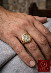 A photo showing a man's hand on a grey cloth surface, wearing the Men's 10K Two-Tone Gold Saint Michael Archangel Signet Ring on the ring finger, highlighting its size, fit, and design details on the hand.