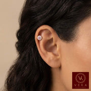 Close-up of an ear cartilage piercing a pink gemstone earring with Veka logo.