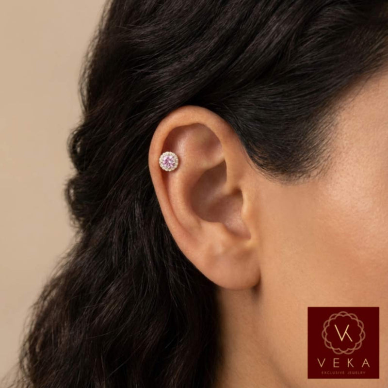 Close-up of an ear cartilage piercing a pink gemstone earring with Veka logo.