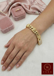 Woman wearing a thick 15mm 10K yellow gold Cuban link bracelet with Medusa head details and a sparkling CZ clasp on her wrist